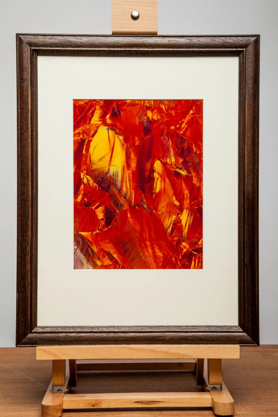 Gerahmtes abstraktes Bild mit roten und orangefarbenen Flächen und hellgelben Linien.