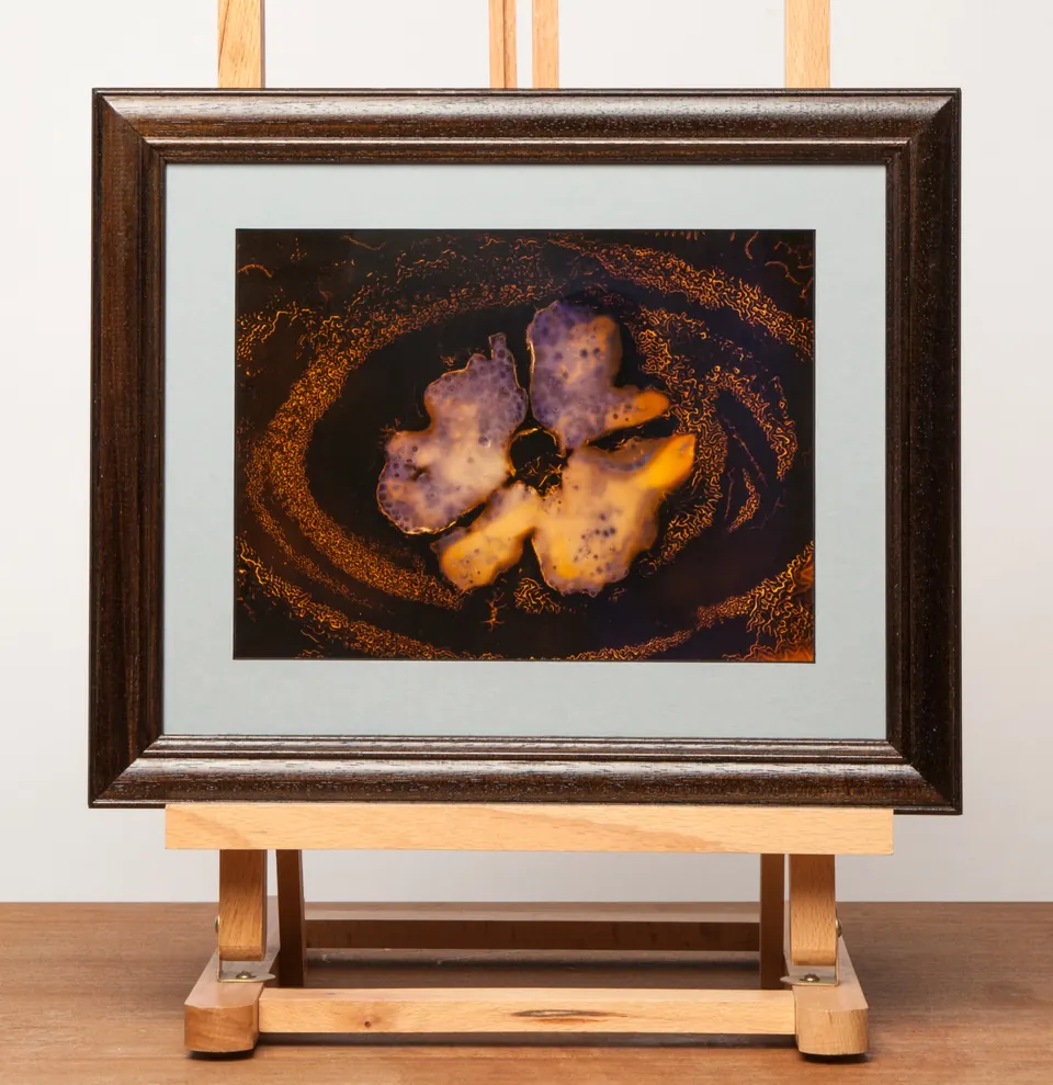 Gerahmtes abstraktes Bild mit orangefarbenen und violetten geschwungenen Formen auf dunklem Grund.