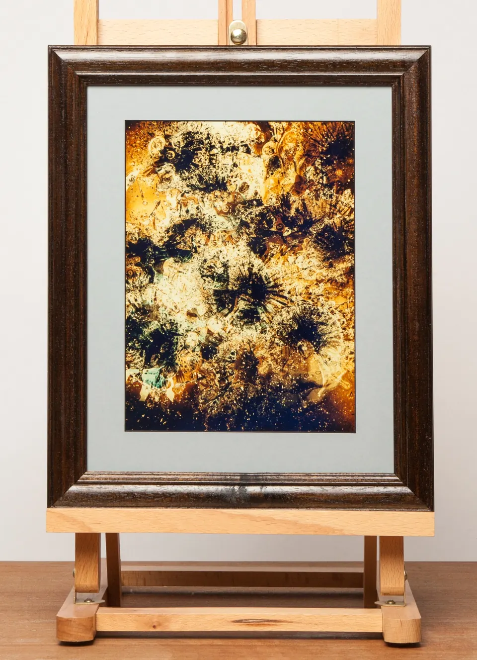 Gerahmtes abstraktes Bild mit dichten goldenen Strukturen und dunklen runden Formen.