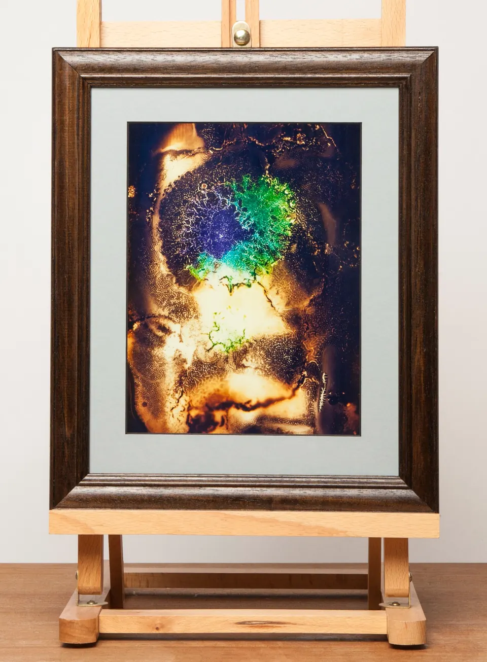 Gerahmtes abstraktes Bild mit hellgelben Flächen um eine grüne und blaue runde Form.